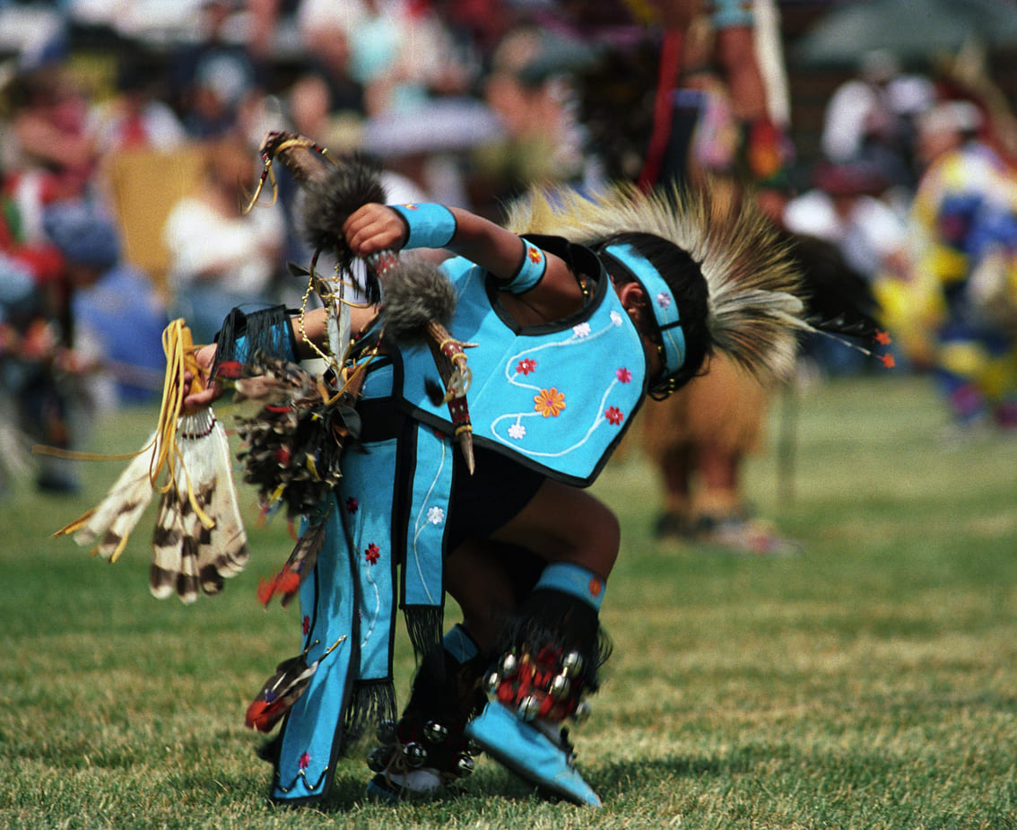 A young artist dressed in traditional Native American attire dances at a powwow, showcasing cultural pride and heritage.