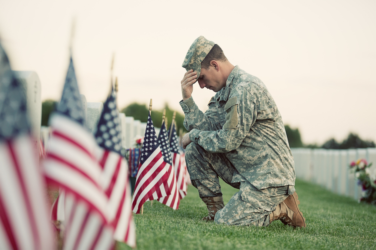 A soldier kneels beside graves adorned with American flags, honoring fallen heroes on Memorial Day.