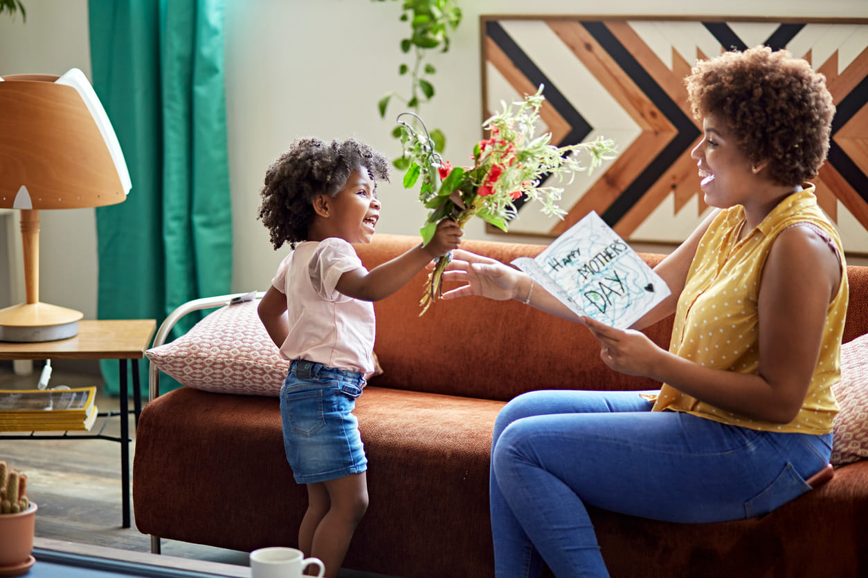 A joyful child presents her mother with flowers and a homemade Mother's Day card, capturing a heartfelt moment.