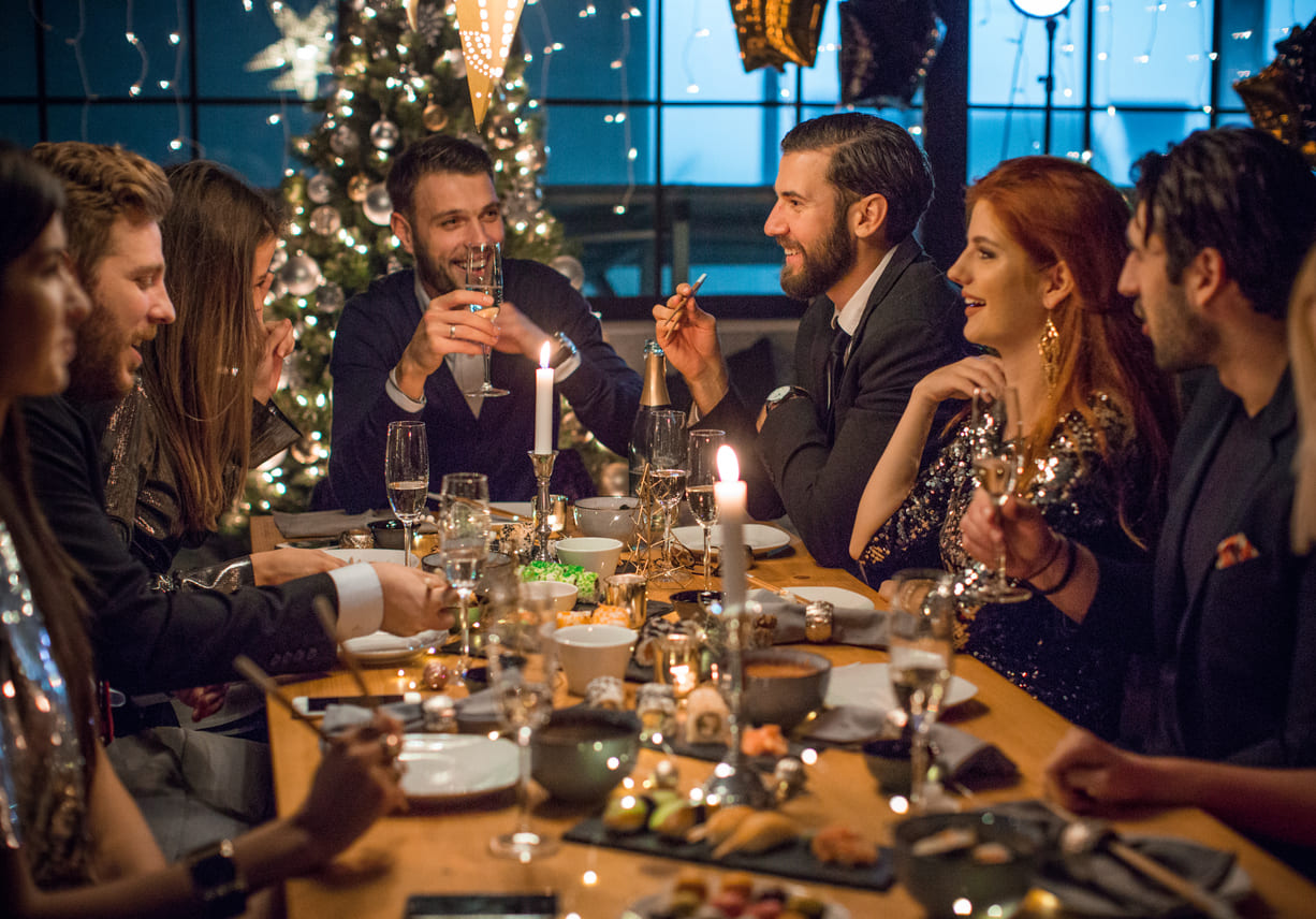 A group of friends enjoys a lively New Year's Eve dinner, surrounded by festive lights and cheerful conversation.