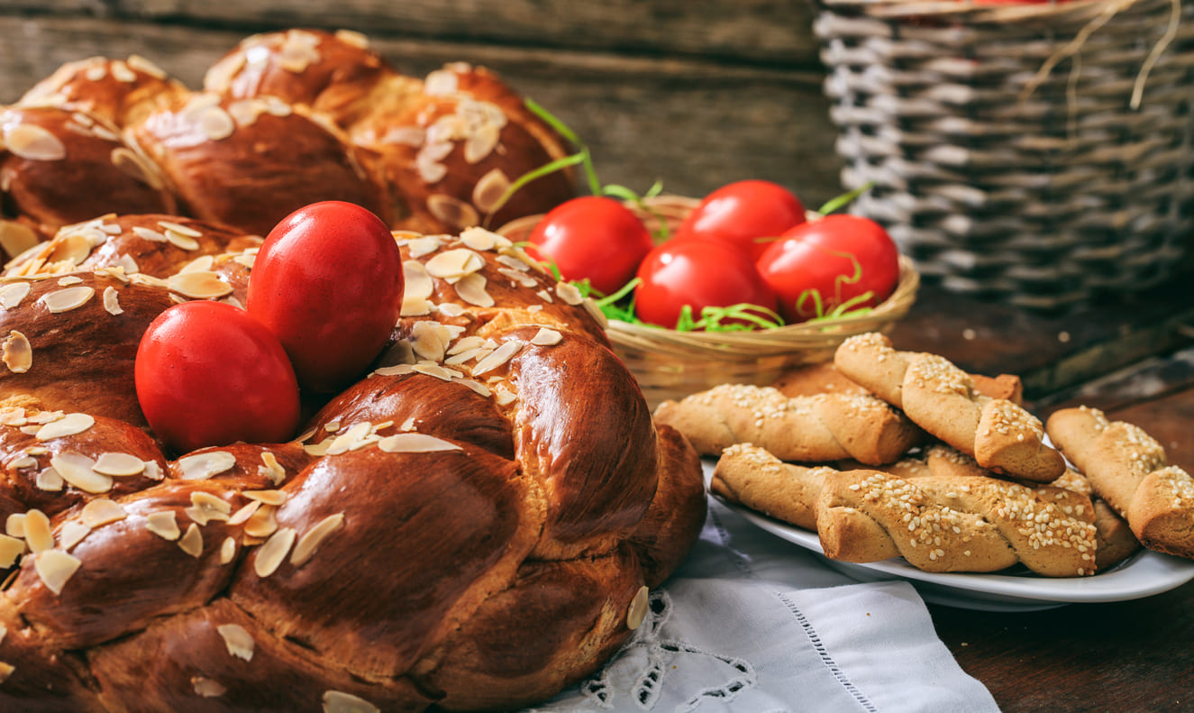 Tsoureki, a traditional sweet bread with red-dyed eggs, alongside festive treats prepared for Orthodox Easter celebrations.