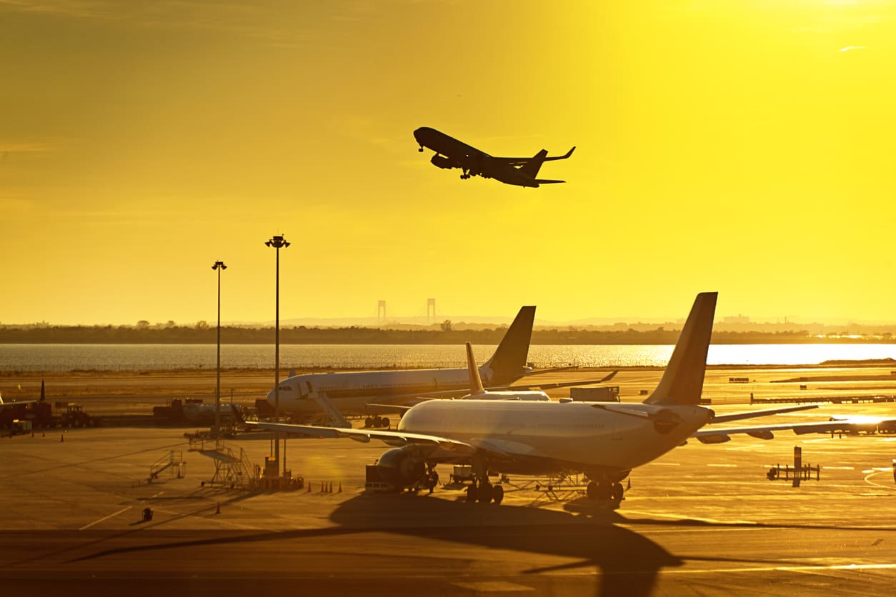 An airport at sunset, with planes parked on the runway and one taking off, reflecting the spirit of aviation.