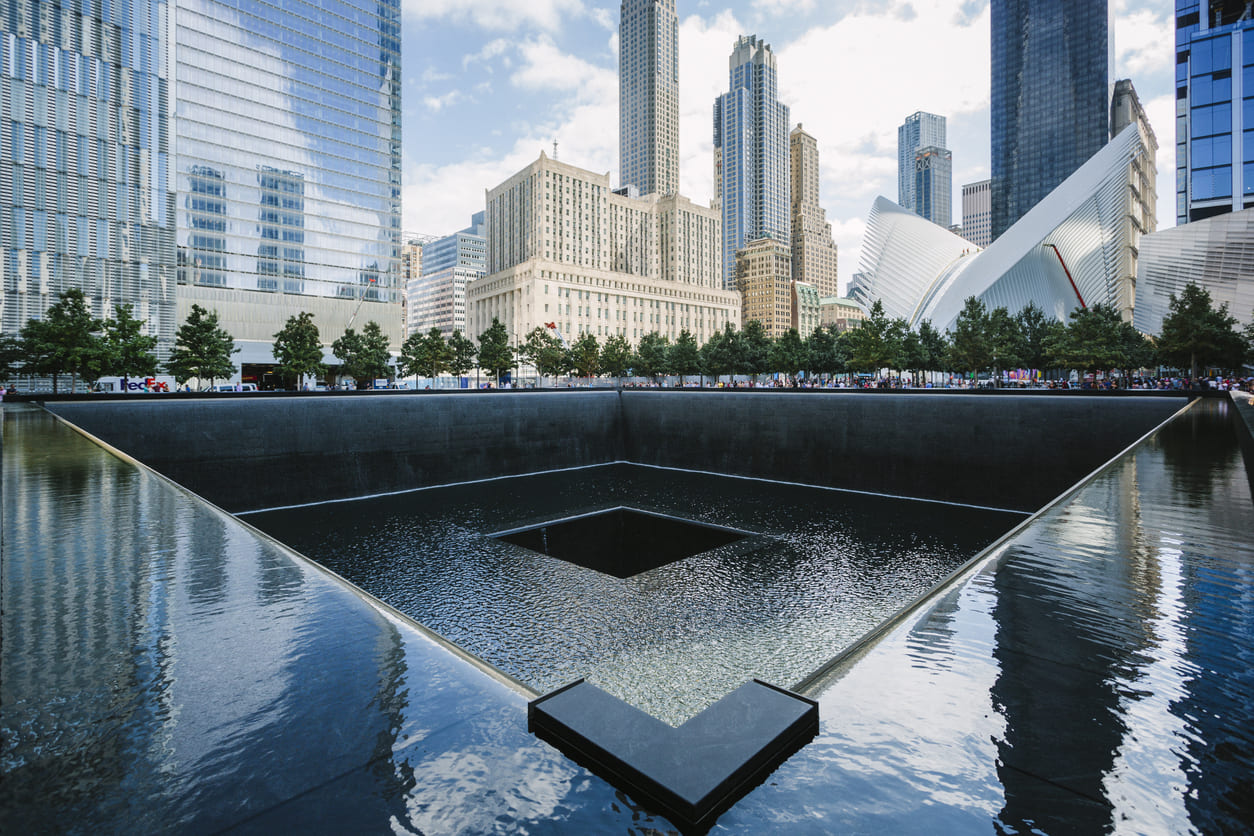 9/11 Memorial in New York City, featuring a serene reflecting pool surrounded by trees, set against the backdrop of modern skyscrapers.