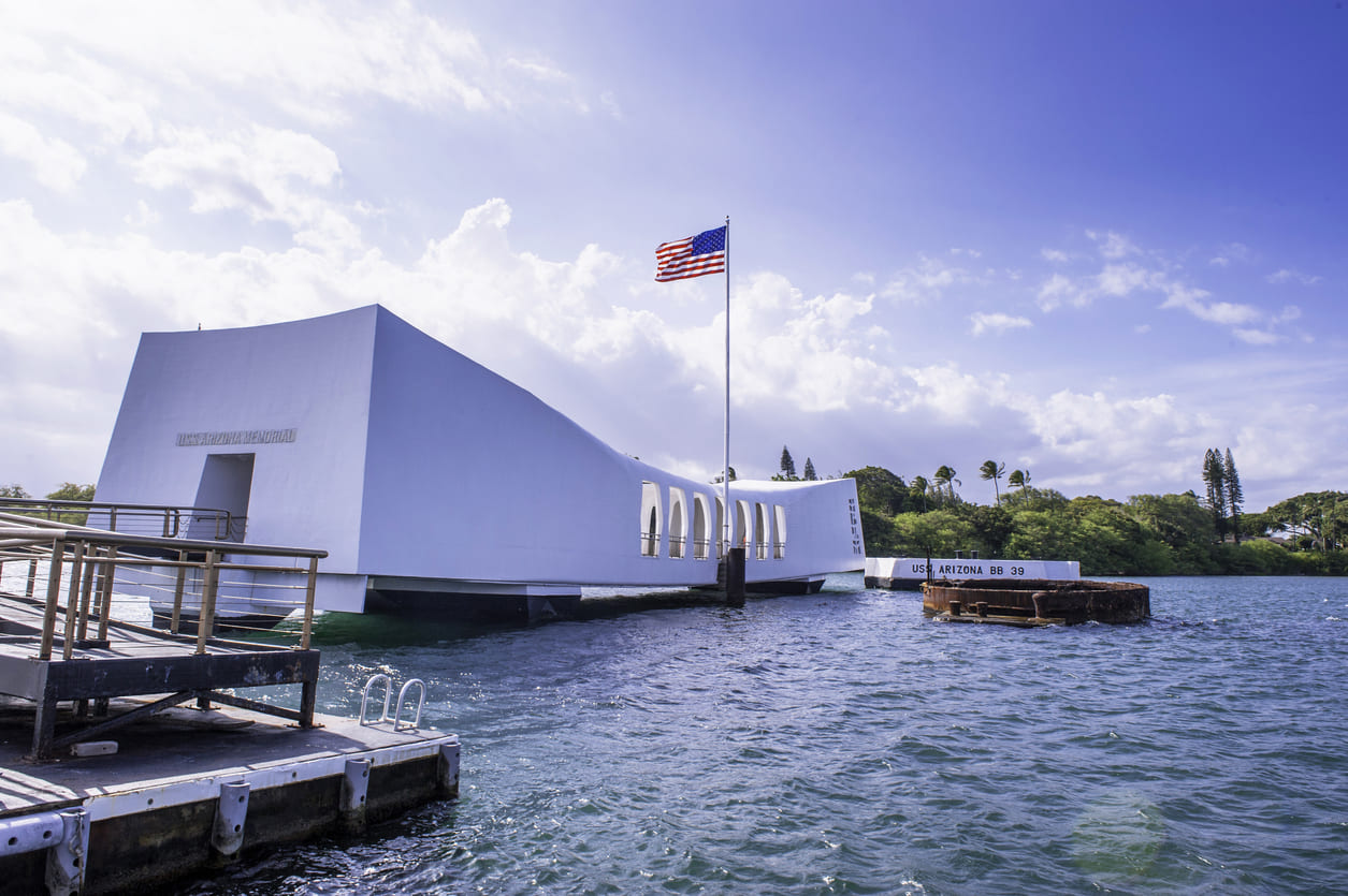 USS Arizona Memorial, a white structure spanning the sunken battleship, with the American flag flying above.