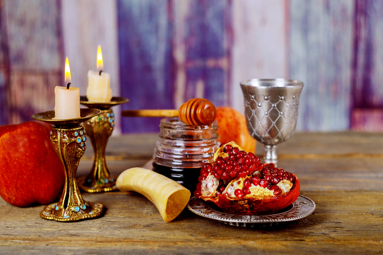 A Rosh Hashanah arrangement featuring candles, honey, pomegranate, and a shofar, representing traditions and blessings for the Jewish New Year.