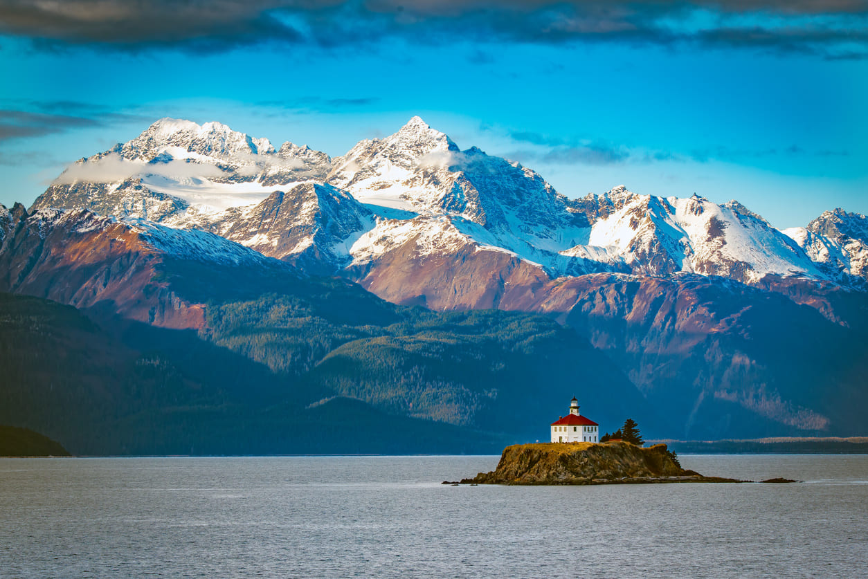 Iconic Eldred Rock Lighthouse, standing tall against the backdrop of rugged Alaskan coastline and snow-capped mountains.