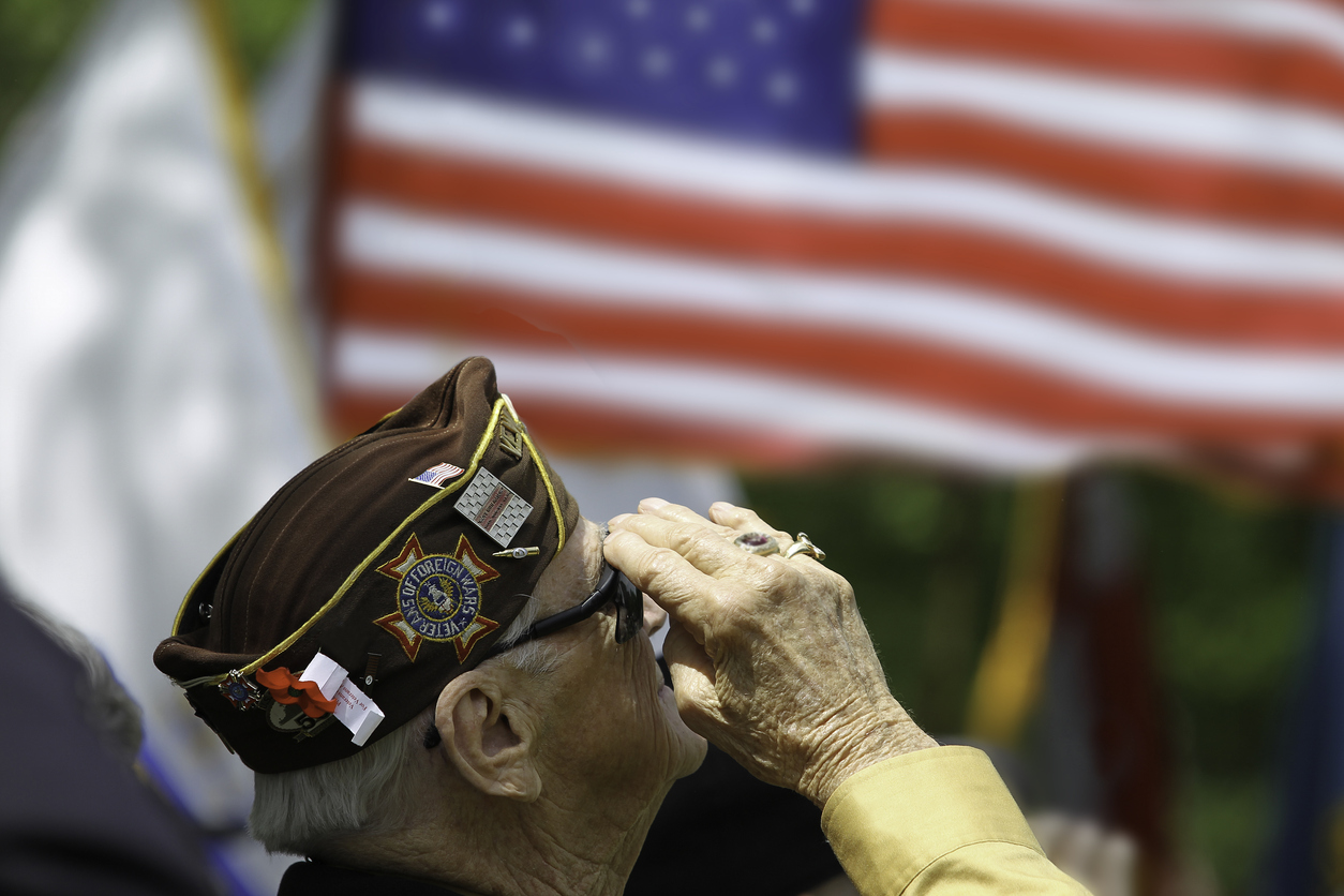 An elderly veteran salutes proudly in front of the American flag, honoring Veterans Day.