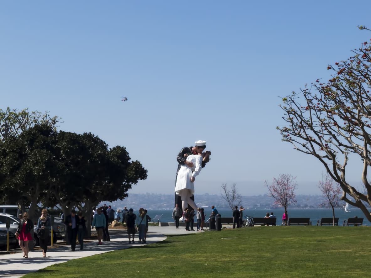 A large statue depicting the iconic sailor kissing a nurse stands in a park setting, symbolizing the celebration and relief of World War II's end.