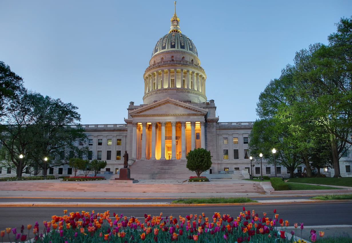 West Virginia State Capitol, beautifully illuminated and surrounded by vibrant flowers, symbolizing the state's history and pride.