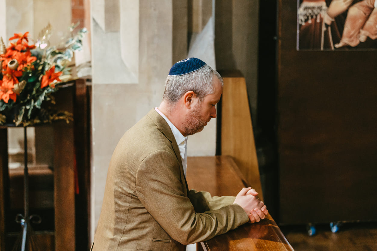 A man wearing a kippah prays in quiet reflection at a synagogue, embodying the solemnity of Yom Kippur.