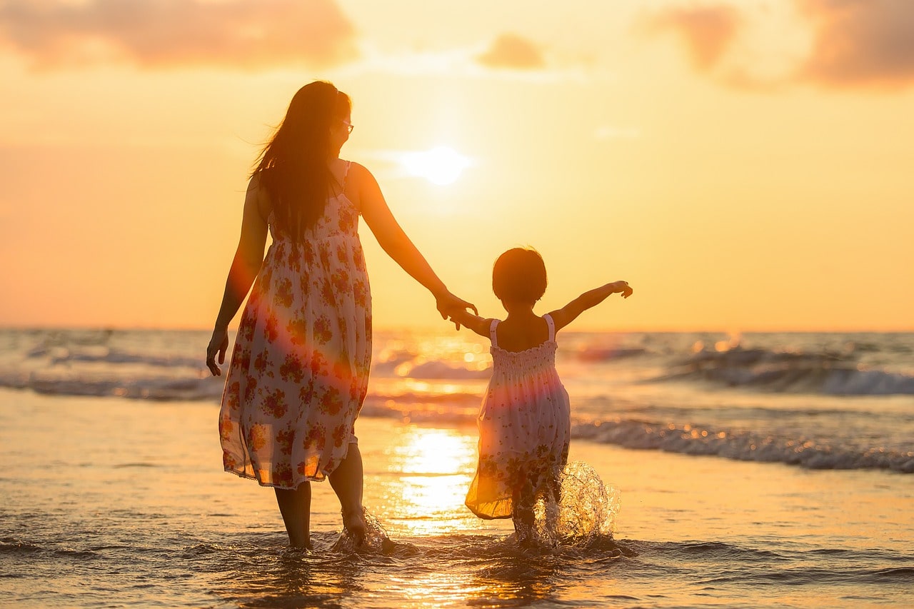 A mother and her daughter enjoy the warm glow of the evening sun on a beach.