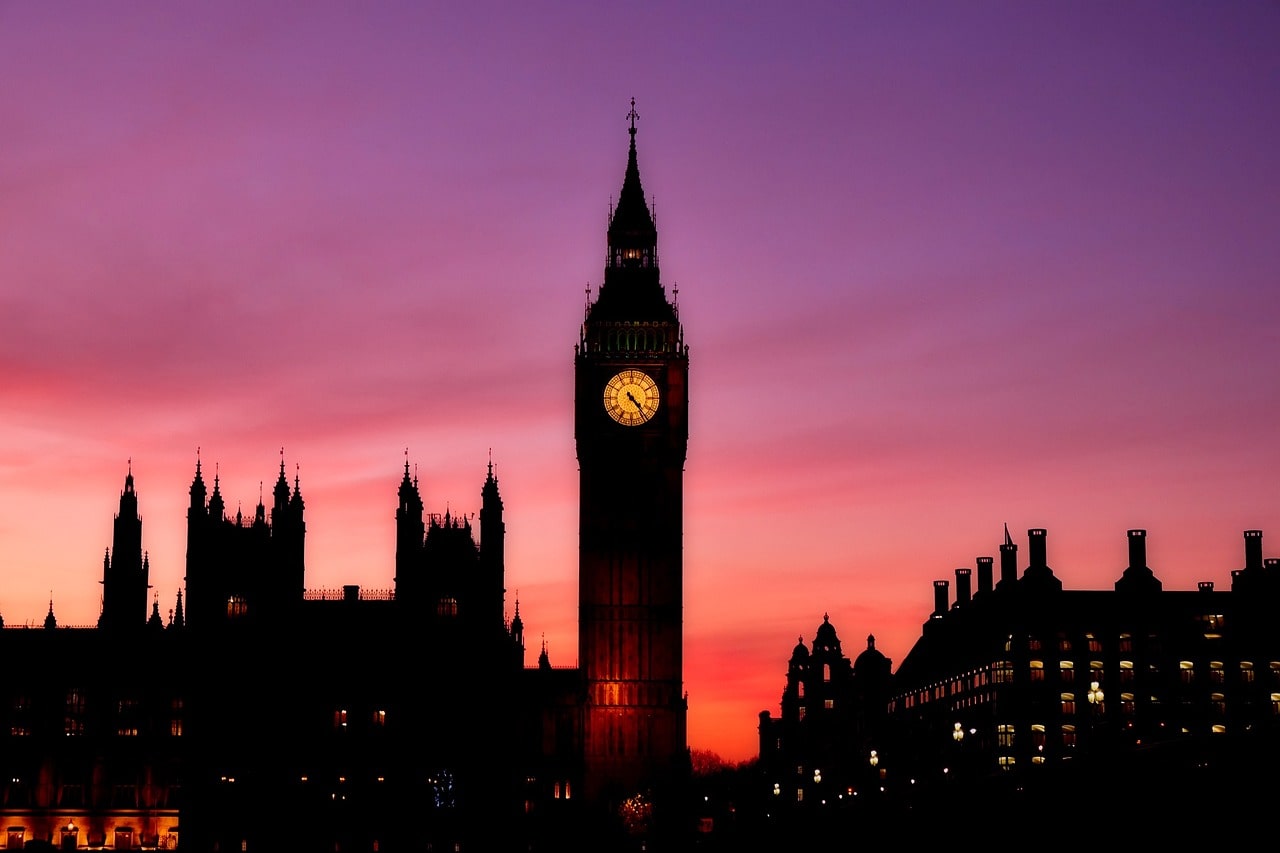 Big Ben with its clock glowing against a city evening view, under a pink sky.